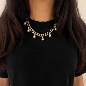 Guldpläterat halsband med droppformade pärlor - Elegant halsband i guldpläterat rostfritt stål – finns även i silverfärgad variant. Matchande örhängen finns i en separat annons.  Smycket är 9 mm brett och har en justerbar längd mellan 38–43 cm, vilket gör att det passar perfekt oavsett stil och tillfälle.. De nickelfria och handgjorda