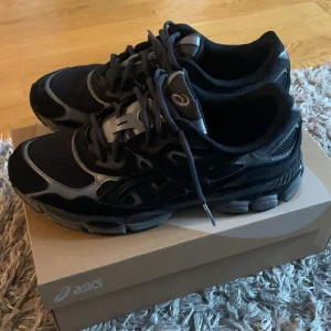 Svarta och grå Asics sneakers - Säljer ett par snygga Asics sneakers i svart och grått med mesh och syntetdetaljer. Skorna har rund tå, platt sula och snörning. Perfekta för dig som gillar sportig stil och vill ha bekväma skor till vardagen. Klassisk Asics-logga på sidan. Köpta från JD och är som helt ny då jag använt de en gång för att testa.