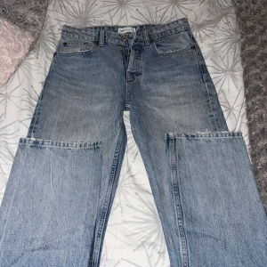 Blå wide jeans från Zara - Säljer ett par ljusblå jeans från Zara med breda ben och råa, avklippta kanter vid knäna för en edgy look. Klassisk femficksmodell med hög midja och knappgylf. Perfekt för dig som gillar statement-plagg och streetstyle. Jeansen har en rak passform ner till benen