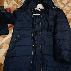 Mörkblå pufferjacka med huva  - Mörkblå pufferjacka från H&M i storlek XS. Jackan har huva med fuskpäls, dragkedja framtill, snörning i midjan och två fickor med dragkedja. Perfekt för kalla dagar och riktigt skön att bära.