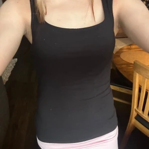 Svart linnetopp från 157, storlek S - En svart, tight och basic linnetopp från 157 med breda axelband och fyrkantig ringning. Tillverkad i mjuk och stretchig viskosblandning som sitter snyggt mot kroppen. Perfekt att styla med jeans eller kjol för en clean look.