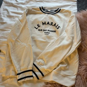 Vit sweatshirt Le Marais Paris M - Vit sweatshirt med svart text 'Le Marais Rue des Rosiers Paris 1983' på bröstet. Svarta ränder på krage och muddar ger en sportig vibe. Rund hals och långärmad, tillverkad i mjuk bomull. Perfekt för chill dagar och enkel att matcha med jeans eller leggings. Pris går att diskuteras 💞 aldrig använd 