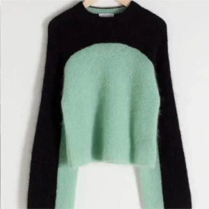 Mintgrön och svart croppad stickad tröja - Säljer en croppad stickad tröja i mintgrönt och svart. Tröjan har långärmade svarta ärmar och en mintgrön kropp med rund hals. Materialet är fluffigt och mjukt, perfekt för att ge en chill vibe till din outfit. Passar dig som gillar att sticka ut med färgblockad design.