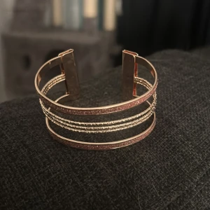 Glittrigt guldigt armband - Snyggt armband i guldton med glittriga detaljer och flera tunna band som ger en cool och modern look. Perfekt för dig som gillar att sticka ut med accessoarer. Armbandet har en öppen design som gör det enkelt att ta på och av. Använd 1 gång