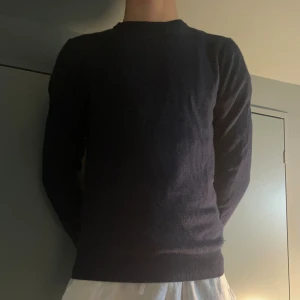 John Henric Kashmir - En stilren mörkblå stickad tröja med rund hals och långärmad passform. Tröjan har en enkel design utan mönster eller detaljer, vilket gör den lätt att matcha med olika outfits. Materialet är mjukt och skönt mot huden, perfekt för kyligare dagar. Litet hål vid armhålan