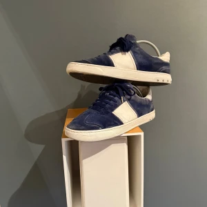 Valentino Flycrews Mörkblå/Vit - Snygga sneakers från Valentino Garavani i blå mocka och vitt skinn. Klassisk låg modell med snörning och coola nitar på sulan. Skick 8/10, finns små fläckar på mockan som ses på bilderna, men enkelt att rusta upp för den som orkar. Box medföljer ej. Priset ej hugget i sten! Vid frågor är det att bara höra av sig.✌️
