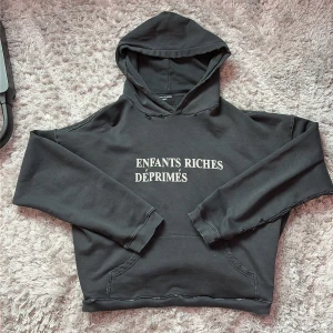 ERD Svart hoodie från Enfants Riches Déprimés - Svart hoodie från ERD / Enfants Riches Déprimés med vit text på bröstet. Tröjan har en rå och edgy look med slitna detaljer vid sömmarna, huva och känguruficka. Tillverkad i 100% bomull för skön komfort. Perfekt för dig som gillar rare streetwear med attityd. ❗️Den är storlek S, men den är såppas översized/baggy att den sitter som typ M eller L (en bra baggy look) Har några små fläckar som knappt syns