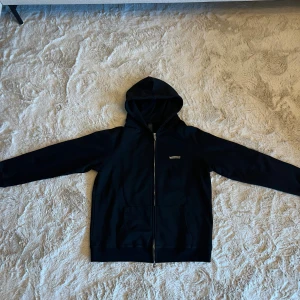 Chrome Hearts, svart hoodie - Svart hoodie från Chrome Hearts med huva och hel dragkedja. Snygga silvriga detaljer och logga på bröstet samt stort tryck med kors och text på ryggen. Mjuk bomullskvalitet och praktisk ficka framtill. Perfekt för dig som gillar designer och chrome hearts