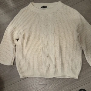 Krämvit stickad tröja från H&M - Mysig krämvit stickad tröja från H&M i storlek XS. Tröjan har ett snyggt flätmönster framtill, ribbade muddar och en lite boxig passform. Perfekt för lager-på-lager och chill höst- och vinterstil.