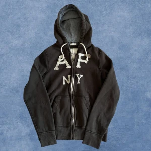 Abercrombie Fitch Hoodie - Säljer nu denna väldigt snygga och trendiga hoodien från Abercrombie Fitch. Storlek L. Längd: 68, bredd: 49, arm: 66. Modellen är 183, 67kg ish. Skriv vid frågor🙌. Har lite slitningar på tröjan, vilket är en del av designen. Svart/brun.