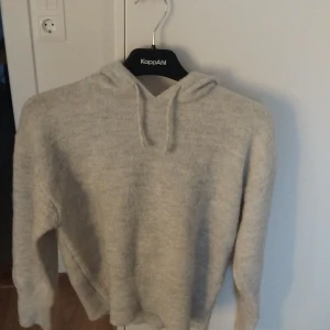 Ljusgrå stickad hoodie från Gina Tricot - Mysig ljusgrå stickad hoodie från Gina Tricot med huva och snörning. Tröjan har lång ärm och är perfekt för kyliga dagar. Enkel och stilren design som passar till det mesta.