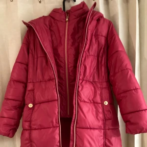 Röd pufferjacka från Michael Kors 11-13 år str 146 cm - Säljer en snygg röd pufferjacka från Michael Kors med guldiga detaljer och dragkedja. Jackan har huva, långa ärmar och quiltad design. Insidan är fodrad med mjukt tyg och har en guldfärgad rand. Perfekt för kalla dagar!