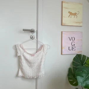 Vit blommig offshoulder topp från NewYorker - Supersöt vit offshoulder topp från NewYorker med ljusrosa blommigt mönster och liten rosett framtill. Tunn och lätt polyester med volangkant vid ärmar och nederkant. Perfekt för dig som gillar romantisk och girly stil! 🌸