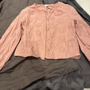 Broderad rosa blus från Dobber - Säljer en söt ljusrosa blus från Dobber i storlek XS. Blusen har broderade blommor över hela tyget, knappar framtill och långärmade puffärmar med resår vid ärmslut. Materialet är mjukt och känns som bomull. Perfekt för dig som gillar romantisk och feminin stil.
