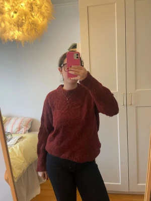 Vinröd stickad tröja med rund hals - Mysig vinröd stickad tröja med rund hals och långa ärmar. Tröjan har en lite loose passform och breda muddar vid ärmslut och nederkant. Perfekt för kyliga dagar och enkel att matcha med jeans eller kjol. Lite stor i storleken. 