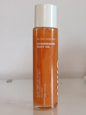 Glow Digger Shimmering Body Oil från Lyko - Glow Digger Shimmering Body Oil från Lyko är en glittrande kroppsolja i en genomskinlig glasflaska med vitt lock. Oljan har en intensiv orange färg med synligt guldskimmer och innehåller macadamia- och mandelolja. Vegansk och lätt doft. Flaskan rymmer 50 ml. Helt oanvänd då jag fick den i min julkalender men vet att jag inte kommer använda den. Är inte äns öppnad.
