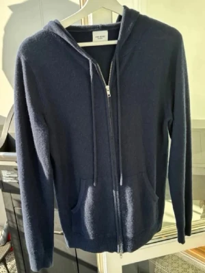 Mörkblå hoodie i kashmir från John Henric  - Snygg mörkblå hoodie från John Henric i 100% Kashmir. Tröjan har dragkedja framtill, huva med snörning och två fickor. Perfekt för dig som vill ha något både stilrent och riktigt mjukt. Klassisk passform och långärmad modell. 