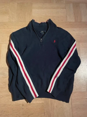 Half zip från Ralph Lauren - Snygg marinblå half zip från Ralph Lauren. Tröjan har half zip, långa ärmar med vita och röda ränder längs sidorna samt en liten röd logga på bröstet. Tröjan är i mycket bra skick. Skriv vid funderingar.