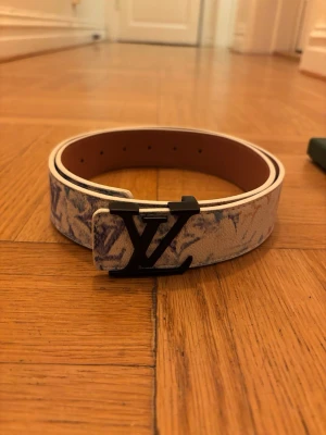 LV bälte special edition - Louis Vuitton bälte i vitt skinn med färgstarkt mönster i blått, orange och gult. Bältet har en stor svart LV-logga som spänne och är tillverkat i spanien, storlek 105. Hör av er vid minsta intresse💸🏌️