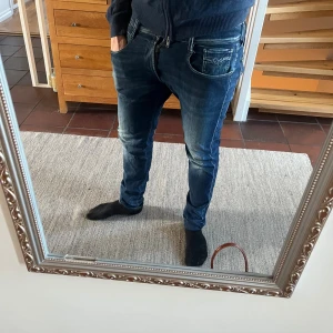 Replay Anbass jeans blå tapered - Säljer ett par snygga Replay Anbass jeans i mörkblå tvätt i storlek 32/34 . Modellen är tapered med normal passform och klassisk femficksdesign. Materialet är stretchigt jeans och de har dragkedja i gylfen.