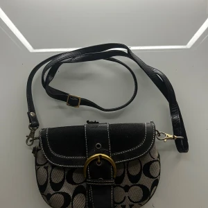 Handväska - Snygg axelväska från Coach med klassiskt monogrammönster i svart och beige. till din outfit. Har ej äktenhestbevis där av det billiga priset och så går lite av lädret av på toppen som lätt kan lagas ❤️❤️Kedjan är även avtagbar.