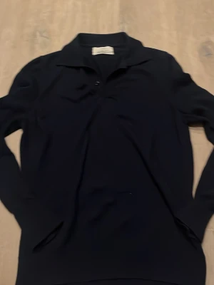 Mörkblå pikétröja från Zara Origins - Säljer en mörkblå långärmad pikétröja från Zara Origins i storlek M. Tröjan har klassisk krage och knäppning framtill, perfekt för en clean och stilren look. Tillverkad i mjukt material som känns skönt mot huden.