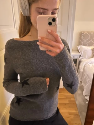 Grå stickad tröja med svarta stjärnor - Mysig grå stickad tröja med svarta stjärnor som detaljer. Tröjan har en lös passform och långa ärmar, samt en bredare halsringning. 