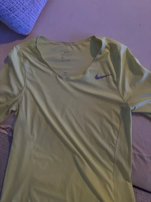 Träningströja  - Bilden visar en ljusgul Nike Dri-Fit träningströja i storlek S, inte en sko. Tröjan har korta ärmar och är tillverkad i ett syntetmaterial som andas, perfekt för sport och träning.