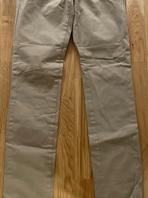 Chinos från Tommy Hilfiger - Snygga beige chinos från Tommy Hilfiger med klassisk rak passform. Byxorna har bälteshällor, knappstängning bak och den ikoniska Hilfiger-loggan ovanför bakfickan. Perfekt för en stilren outfit till festliga tillfällen