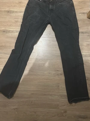 Svarta Jack and Jones jeans  - Svarta jeansbyxor i klassisk rak modell med fem fickor och knappgylf. Byxorna har en enkel design utan synliga detaljer och är tillverkade i slitstarkt jeanstyg. Passar dig som gillar en clean och tidlös look.