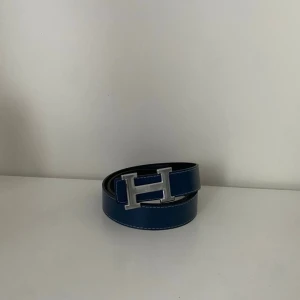 HermesBälte - Snygg blå väst i skinn med stilrena silverfärgade detaljer. Västen har en klassisk form och är helt utan mönster, vilket gör den enkel att matcha med olika outfits. Perfekt för dig som gillar en clean och modern look.Längd 110cm