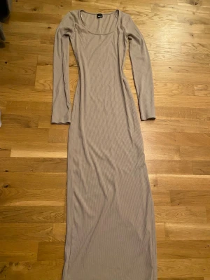 Beige ribbad långklänning - Säljer en beige långklänning med ribbad struktur och lång ärm. Klänningen har en rundad urringning och är figurnära i modellen. Perfekt för dig som gillar stilrena och enkla plagg med en modern touch.