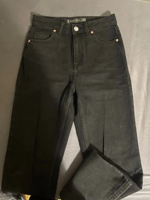 Svarta jeans från Amisu, storlek 36 - Svarta jeans från Amisu i klassisk femficksmodell med raka ben och hög midja. Jeansen har silverfärgad knapp och nitar, samt en enkel design utan mönster. Materialet är jeans och passformen är normal med straight snitt. Perfekt till sneakers eller boots.