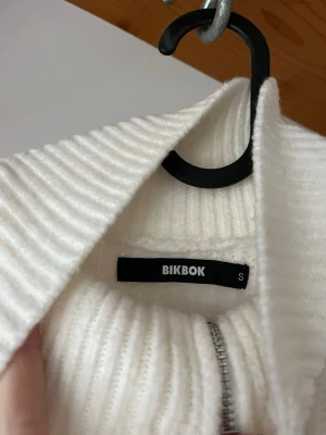Vit ribbad kofta från Bikbok - Säljer en vit ribbstickad kofta från Bikbok i storlek S. Koftan har hög krage, långa ärmar och en snygg dragkedja framtill. Materialet är stickat och ger en mysig känsla, perfekt för kyliga dagar. Knappt använd. 
