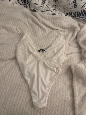 Vit body med v-ringning - Säljer en vit body med v-ringad spets upptill och slät nederdel. Axelbandslös design med tunna axelband och spetsdetaljer som ger en romantisk vibe. Perfekt att styla med jeans eller kjol.