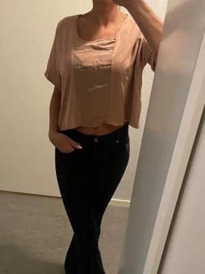 Ljusrosa/beige/brun croppad topp från H&M - Säljer en croppad topp från H&M i storlek XS. Se bild för egen uppfattning av färg. Toppen har korta ärmar, rund halsringning och en lös passform. Materialet är mjukt och lätt, perfekt för varmare dagar. Enkel och stilren design som är lätt att matcha. Olika material för lite liv och mer elegant känsla se bild. Oversize. Passar därför de flesta oavsett storlek 