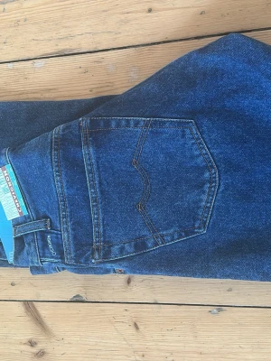 Blå raka jeans från Chevignon W28 - Säljer ett par klassiska blå jeans från Chevignon, modell Dean. Jeansen har rak passform, hög midja och fem fickor. Tillverkade i robust denim med snygga kontrastsömmar och diskret Chevignon-märke på bakfickan. Perfekta för en clean och tidlös look.