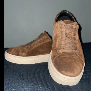 Bruna mockasneakers från Vagabond - Säljer dessa tjusiga Vagabonds pga för små. Brunt mocka material med en naturvit sula. Passar dig som vill ha en stilren och neutral stil men inte för kaxig. Använt lite men finns fof tecken på användning. Skon är storlek 38 men sitter som 39/39,5.      Nypris: 1500kr