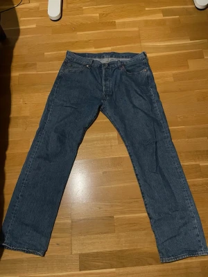 Levi's 501 blå jeans W36 L32 - Klassiska blå Levi's 501 jeans med rak passform och knappgylf. Tillverkade i slitstarkt bomullstyg och har den ikoniska läderlappen bak i midjan. 