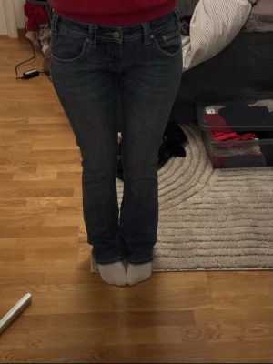 Rock & Roll bootcut jeans med broderi - Bootcut jeans från Rock & Roll som jag köpte second hand i London.i klassisk blå denim med låg midja. Framsidan har slitna detaljer vid knäna och baksidan har snygga broderade mönster på bakfickorna. Perfekt för dig som gillar en avslappnad och cool stil.