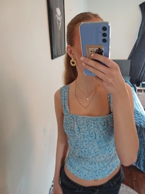 Blommig blå linnetopp med breda axelband - Supersöt ljusblå linnetopp med småblommigt mönster i blått och vitt. Toppen har breda axelband, fyrkantig ringning fram och snyggt skuren rygg. Perfekt till jeans eller kjol för en fräsch sommarkänsla. ❤️