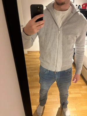 Ljusgrå helzip från Selected Homme - Säljer en stilren ljusgrå kofta från Selected Homme. Tröjan har ribbad krage, muddar och hel dragkedja framtill. Materialet är stickat och ger en soft känsla, perfekt för lager på lager under kyligare dagar.