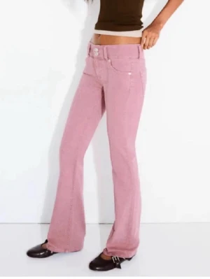 Rosa bootcut jeans från Bershka - Säljer ett par snygga rosa jeans från Bershka , i bra skick. Jeansen har en bootcut passform och är midwaist. Byxorna har dubbla knappar i midjan.
