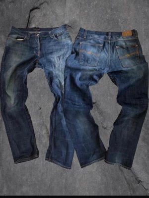 Nudie Jeans Grim Tim blå jeans 34/32 - Säljer ett par klassiska Nudie Jeans Grim Tim i tvättad blå denim. Modellen har raka ben, fem fickor och orange sömmar på bakfickorna. Materialet är 98% bomull och 2% elastan för lite stretch. Snygg slitning och ikonisk Nudie-lapp bak i midjan.