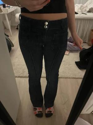 Mörkblå bootcut jeans med fickor - Säljer ett par mörkblå jeans med bootcut-snitt och stora framfickor. Jeansen har , dubbla silverknappar och markerade sömmar längs benen. Används få gånger