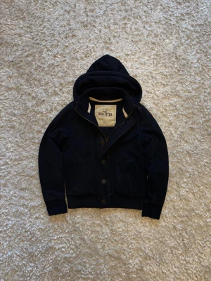Hollister fodrad zip hoodie/cardigan med knappar blå vintage  - Riktigt snygg o varm fodrad kofta från hollister, den är skön o varm perfekt för kylan. Använd men i gott skick förutom lite slitningar som syns på de 2 sista bilderna. Storlek S!