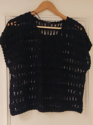 Svart virkad topp från Lindex - Säljer en svart virkad topp från Lindex i storlek M. Toppen har ett grovmaskigt, öppet mönster och är lätt croppad med korta ärmar. Perfekt att styla över ett linne eller bikini för en cool och avslappnad look.