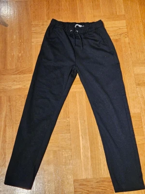 Svarta mjukisbyxor  - Svarta mjukisbyxor med elastisk midja och snörning framtill. Byxorna har raka ben, sidofickor och två bakfickor. Tillverkade i mjukt material som känns skönt mot huden. Perfekta för chill dagar eller när du vill ha det bekvämt.