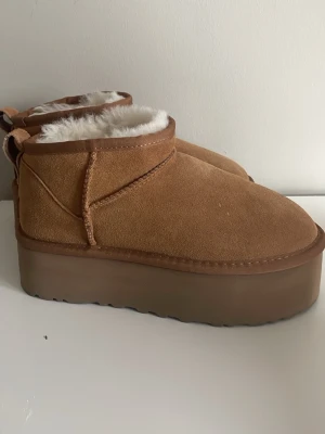 Bruna platå boots med foder - Uggs i  brun/ beige med platå . Skorna är i mocka och har rund tå samt platt sula. Endast använd 2 gånger och passar mig som har storlek 37. Säljer pga att dom ej kommer till användning💕nypris 1500 och vid snabb affär kan jag gå ner i pris💕