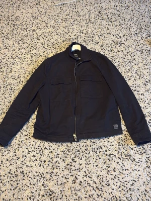Svart overshirt från ZARA - Säljer en svart overshirt från ZARA i storlek L. Jackan har två stora bröstfickor med lock, rak passform och dragkedja framtill. Tillverkad i ett slitstarkt bomullstyg, perfekt för lager på lager under höst och vår. Pris kan givetvis diskuteras 